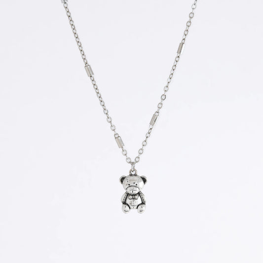 Dainty silver bar link chain with a teddy bear charm for minimalistic fashion or for layering jewelry on a light gray background
