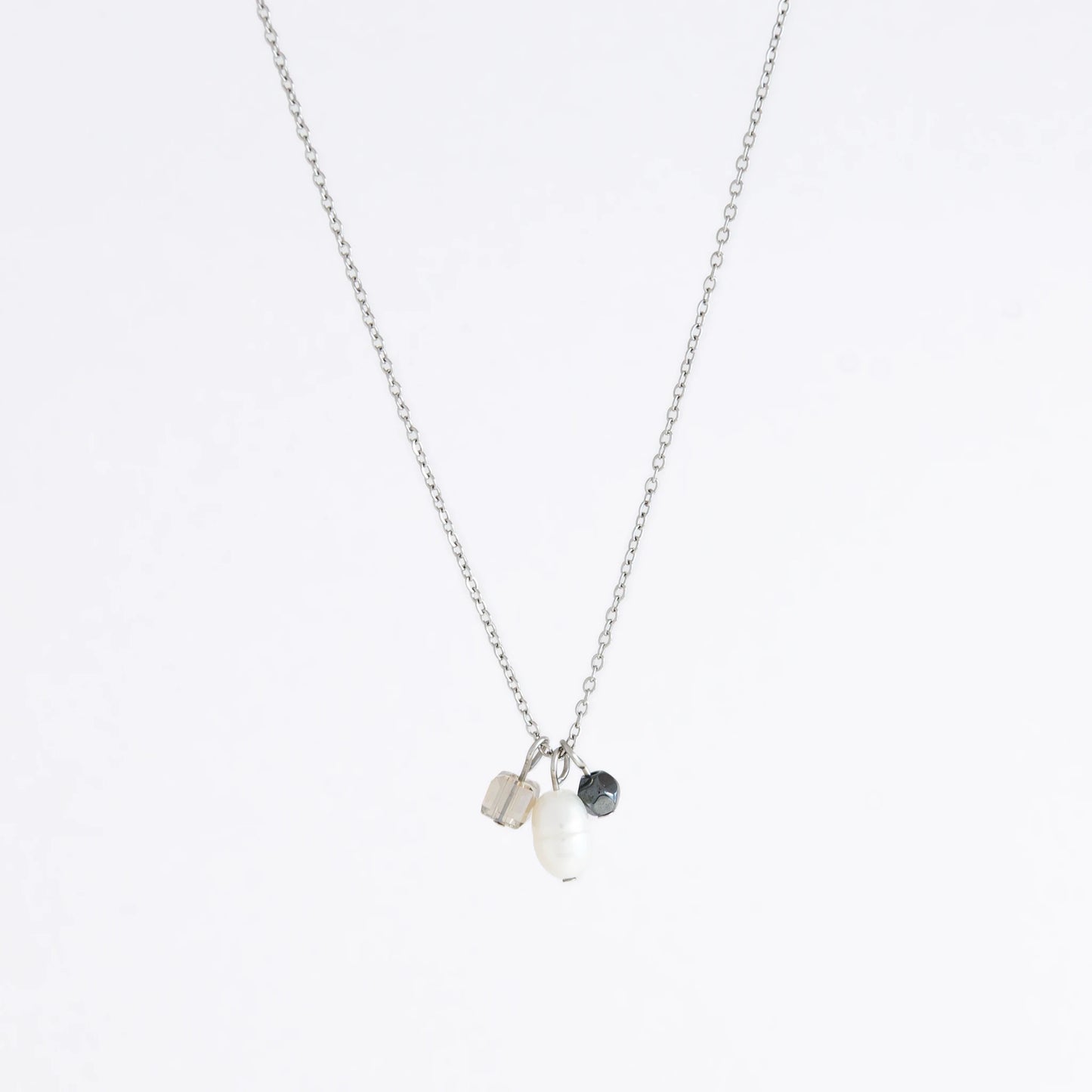 Silver dainty necklace with three small charms made of glass beads and pearls on a white background