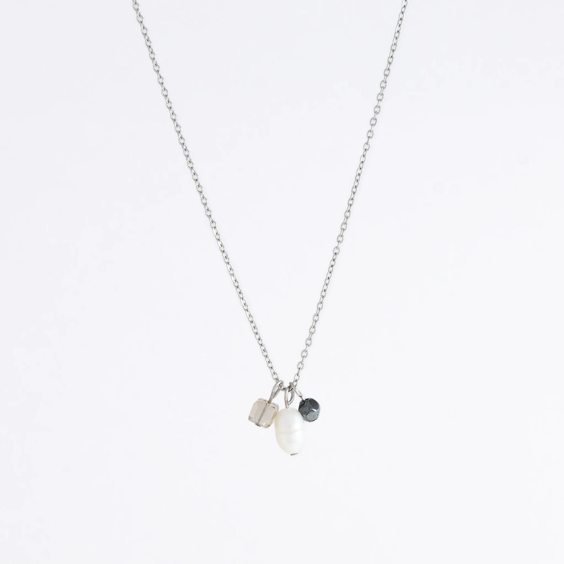 Silver dainty necklace with three small charms made of glass beads and pearls on a white background