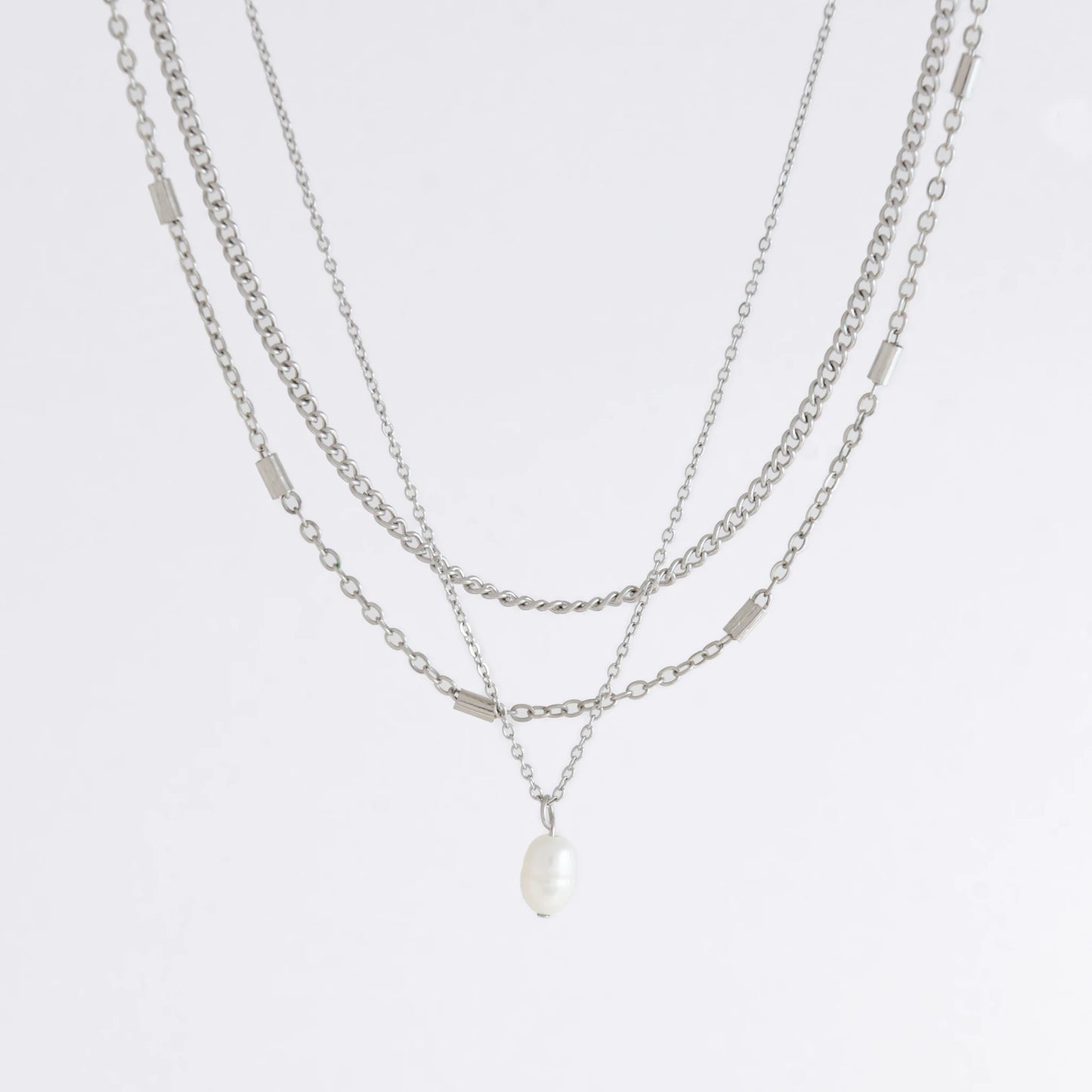 Silver stainless steel layered necklace set with a curb chain, a bar link chain and a dainty pearl pendant necklace on a light gray background