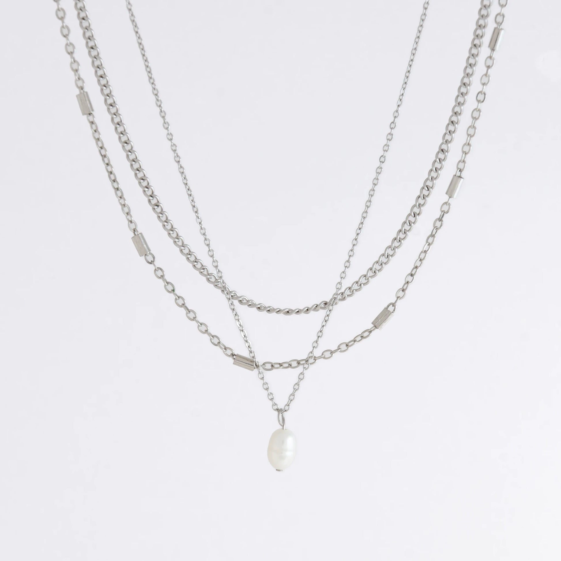 Silver stainless steel layered necklace set with a curb chain, a bar link chain and a dainty pearl pendant necklace on a light gray background