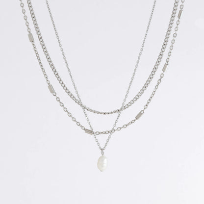 Silver stainless steel layered necklace set with a curb chain, a bar link chain and a dainty pearl pendant necklace on a light gray background