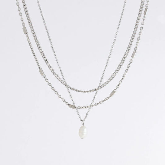Silver stainless steel layered necklace set with a curb chain, a bar link chain and a dainty pearl pendant necklace on a light gray background