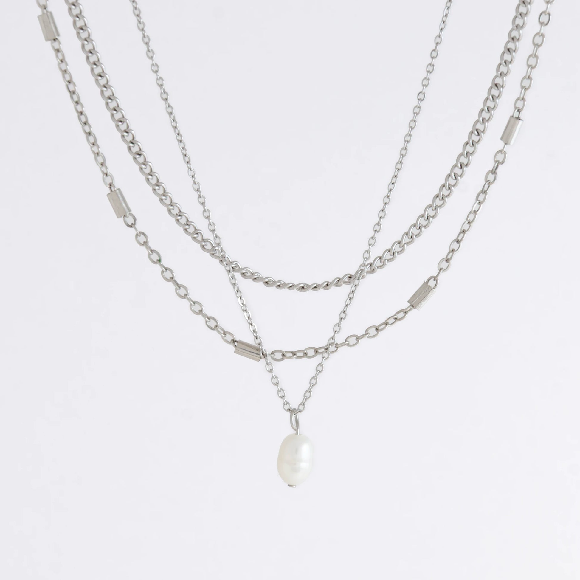 Silver stainless steel layered necklace set with a curb chain, a bar link chain and a dainty pearl pendant necklace on a light gray background