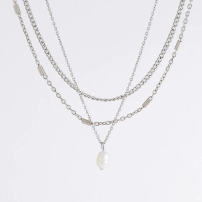 Silver stainless steel layered necklace set with a curb chain, a bar link chain and a dainty pearl pendant necklace on a light gray background