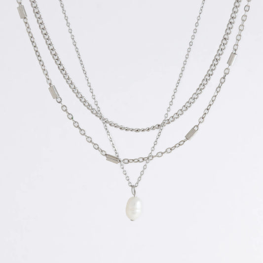 Silver stainless steel layered necklace set with a curb chain, a bar link chain and a dainty pearl pendant necklace on a light gray background