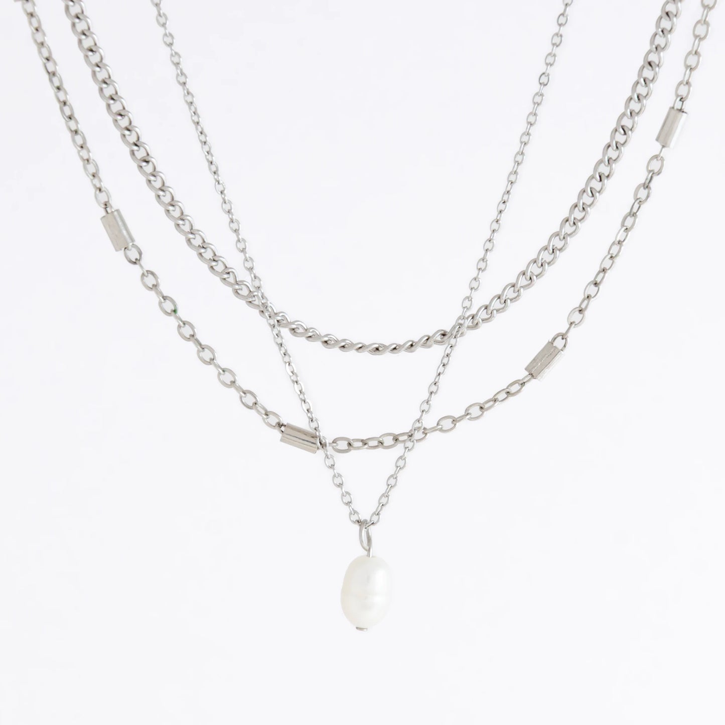 Silver stainless steel layered necklace set with a curb chain, a bar link chain and a dainty pearl pendant necklace on a light gray background