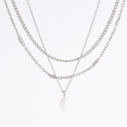 Silver stainless steel layered necklace set with a curb chain, a bar link chain and a dainty pearl pendant necklace on a light gray background