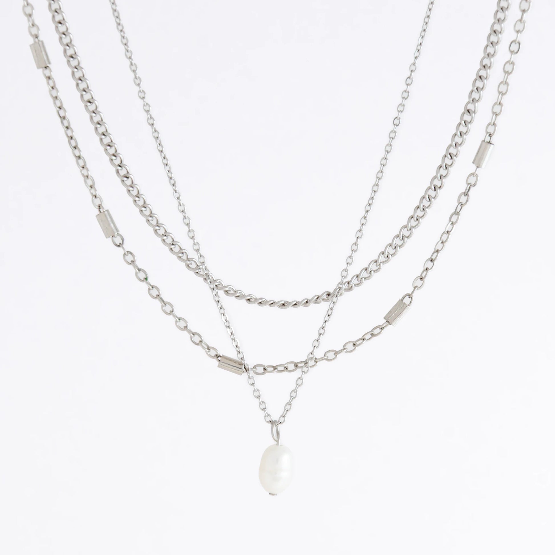 Silver stainless steel layered necklace set with a curb chain, a bar link chain and a dainty pearl pendant necklace on a light gray background
