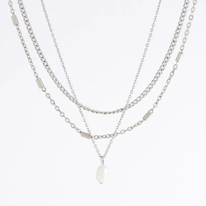 Silver stainless steel layered necklace set with a curb chain, a bar link chain and a dainty pearl pendant necklace on a light gray background