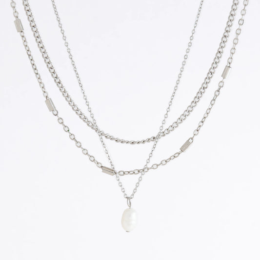 Silver stainless steel layered necklace set with a curb chain, a bar link chain and a dainty pearl pendant necklace on a light gray background