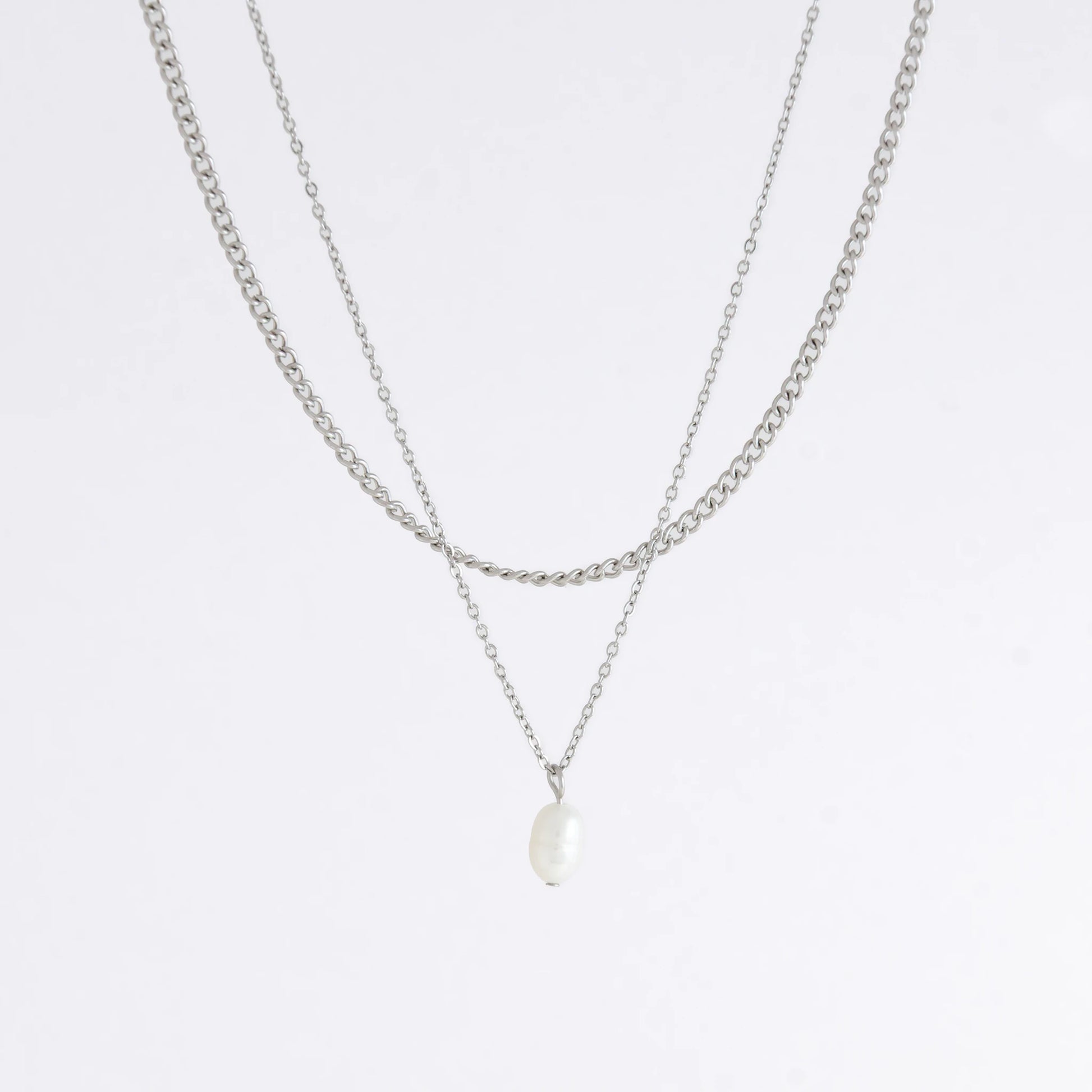 Silver stainless steel layered necklace set with a curb chain and a dainty pearl pendant necklace on a light gray background