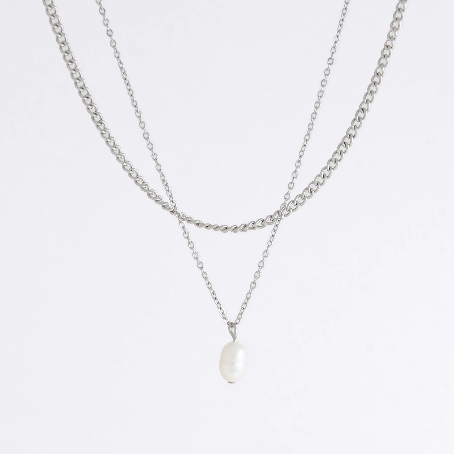 Silver stainless steel layered necklace set with a curb chain and a dainty pearl pendant necklace on a light gray background