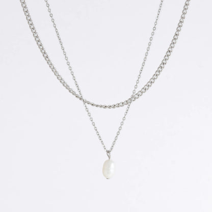 Silver stainless steel layered necklace set with a curb chain and a dainty pearl pendant necklace on a light gray background