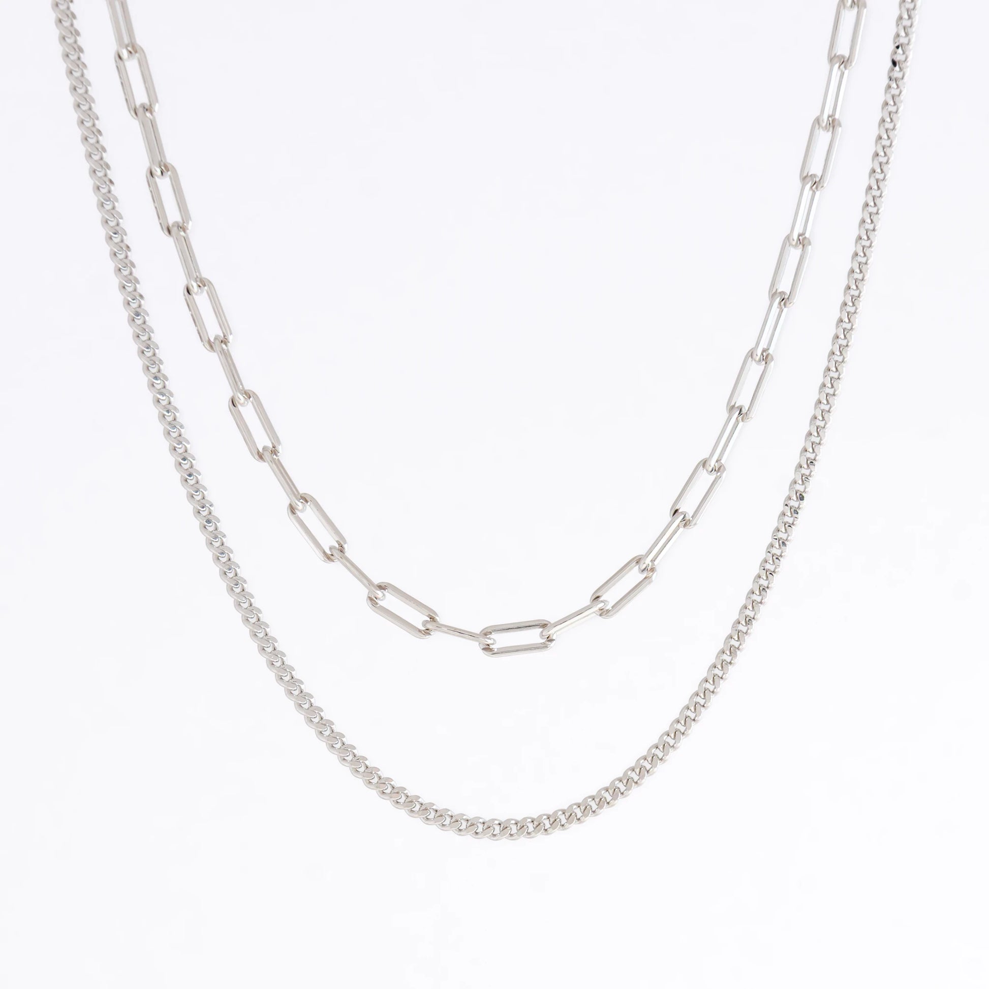 Silver curb chain necklace layered with paperclip necklace on a light gray background