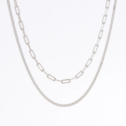 Silver curb chain necklace layered with paperclip necklace on a light gray background