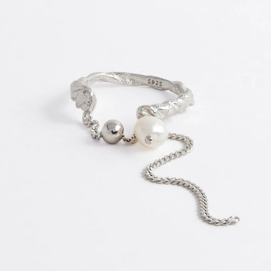Textured ring with pearl and chain detail on a light gray background