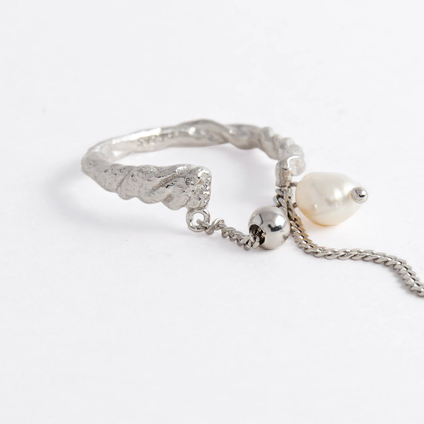 Textured ring with pearl and chain detail on a light gray background