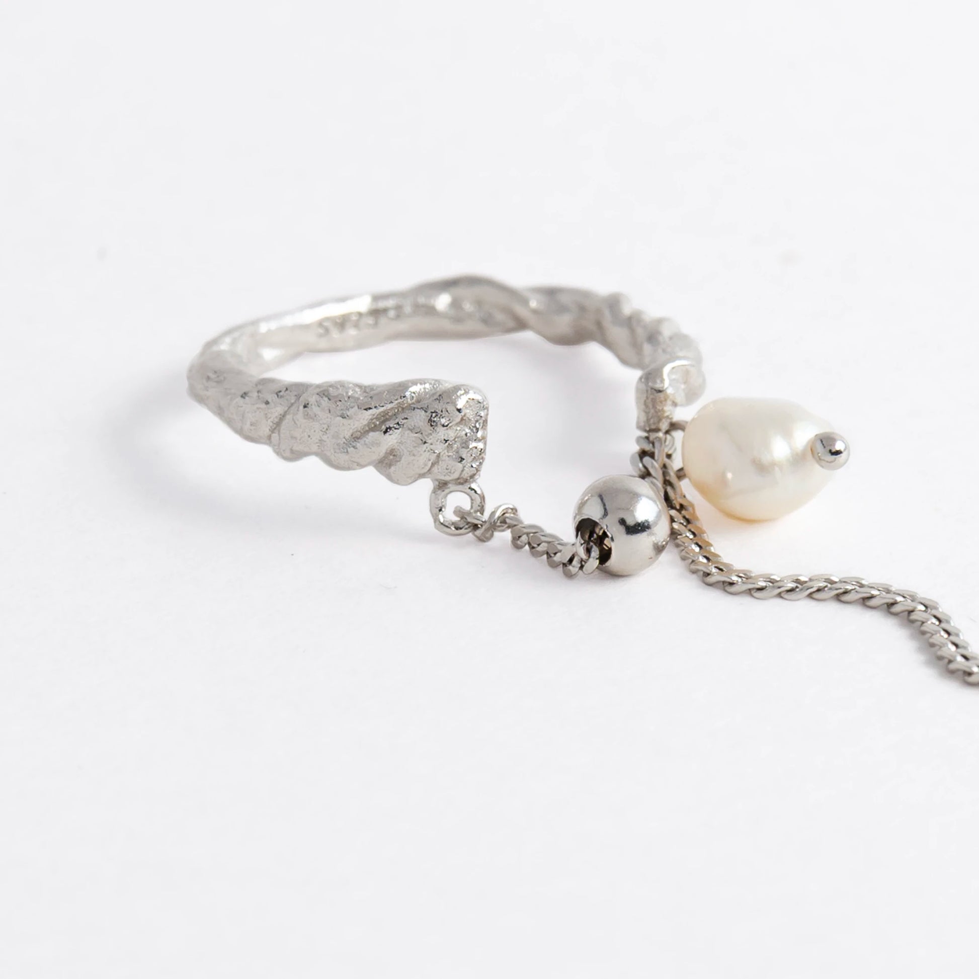 Textured ring with pearl and chain detail on a light gray background