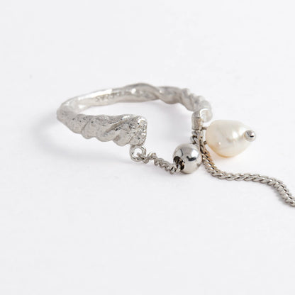 Textured ring with pearl and chain detail on a light gray background