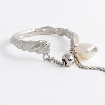 Textured ring with pearl and chain detail on a light gray background