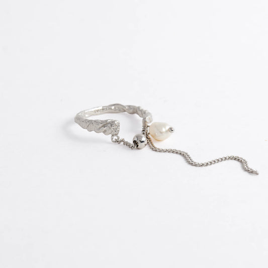Textured ring with pearl and chain detail on a light gray background