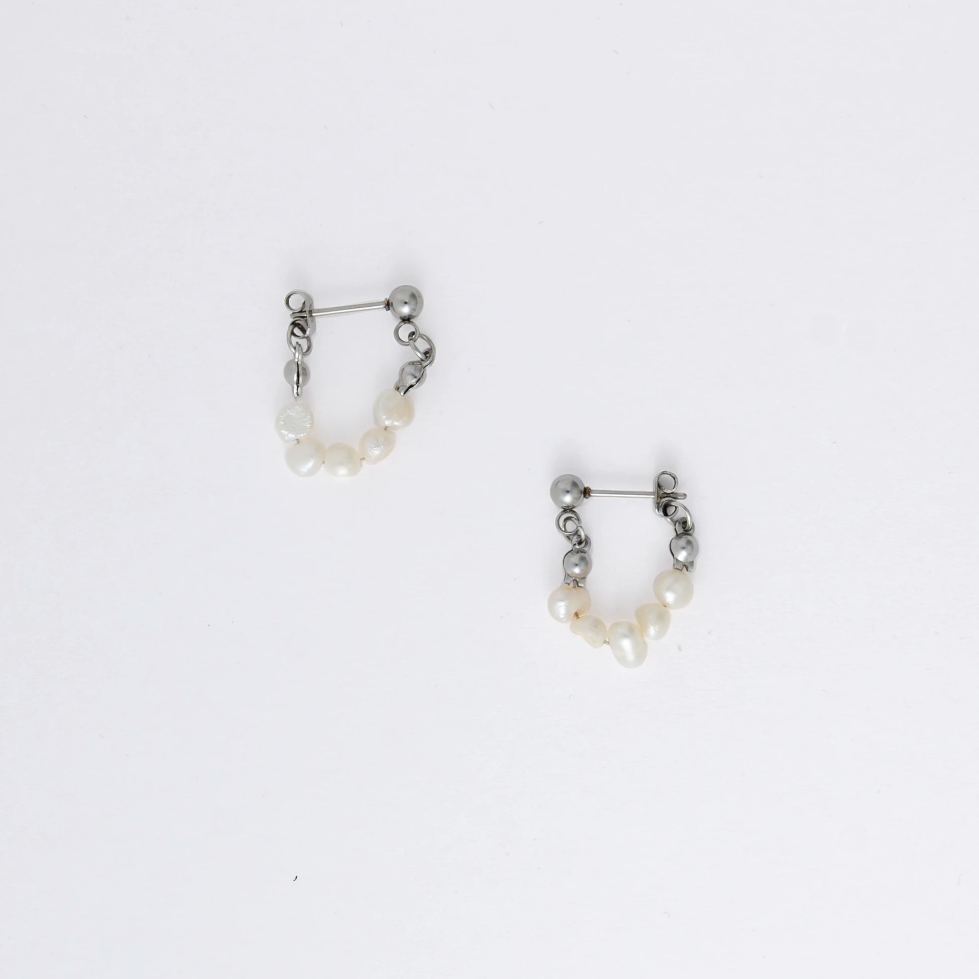 A pair of silver-colored thin pearl hoop earrings, displayed against a white background