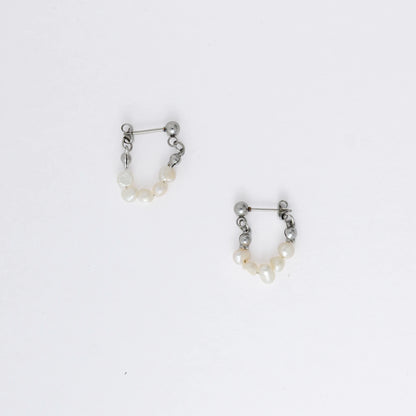 A pair of silver-colored thin pearl hoop earrings, displayed against a white background