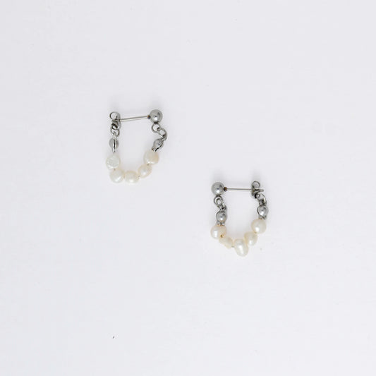 A pair of silver-colored thin pearl hoop earrings, displayed against a white background