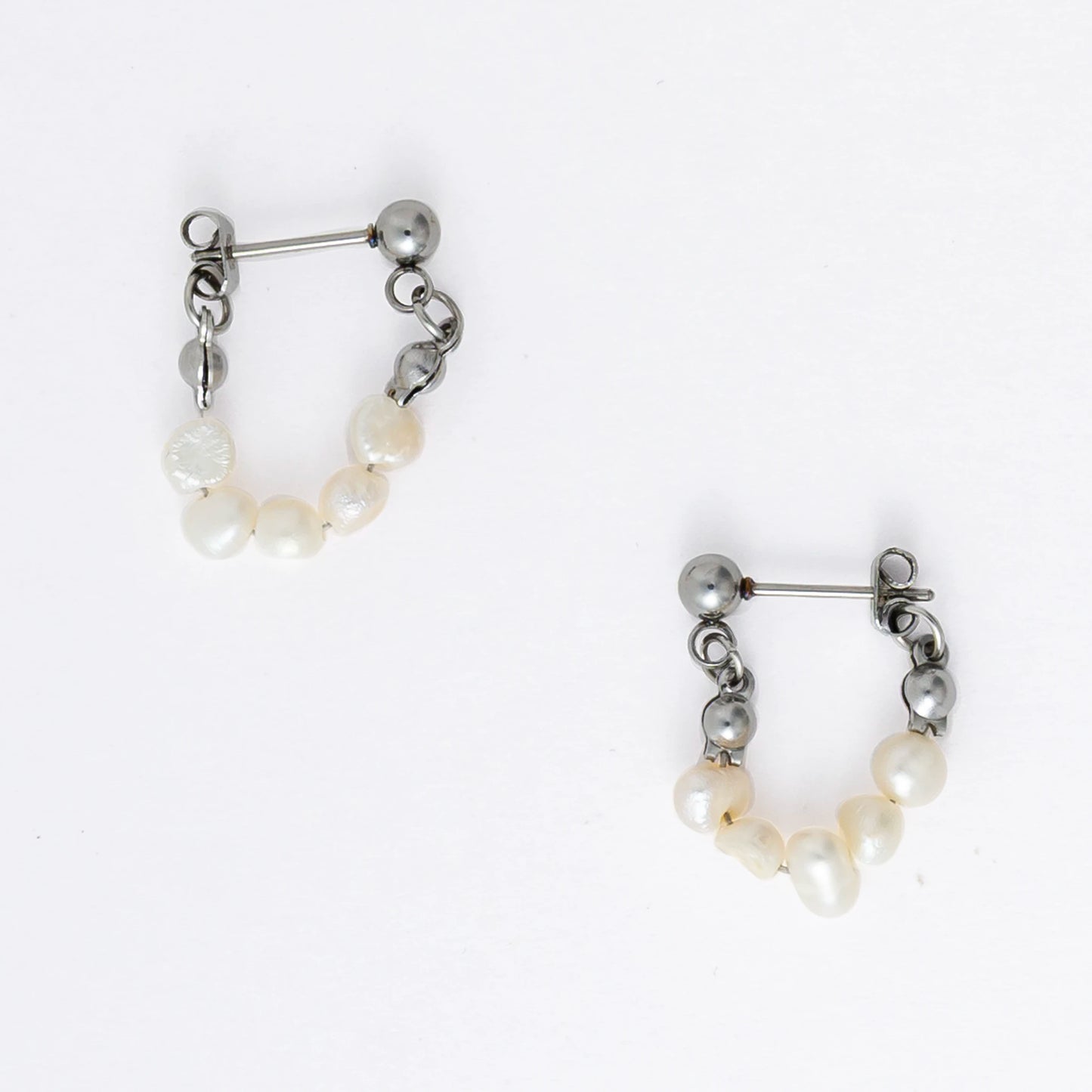 A pair of silver-colored thin pearl hoop earrings, displayed against a white background