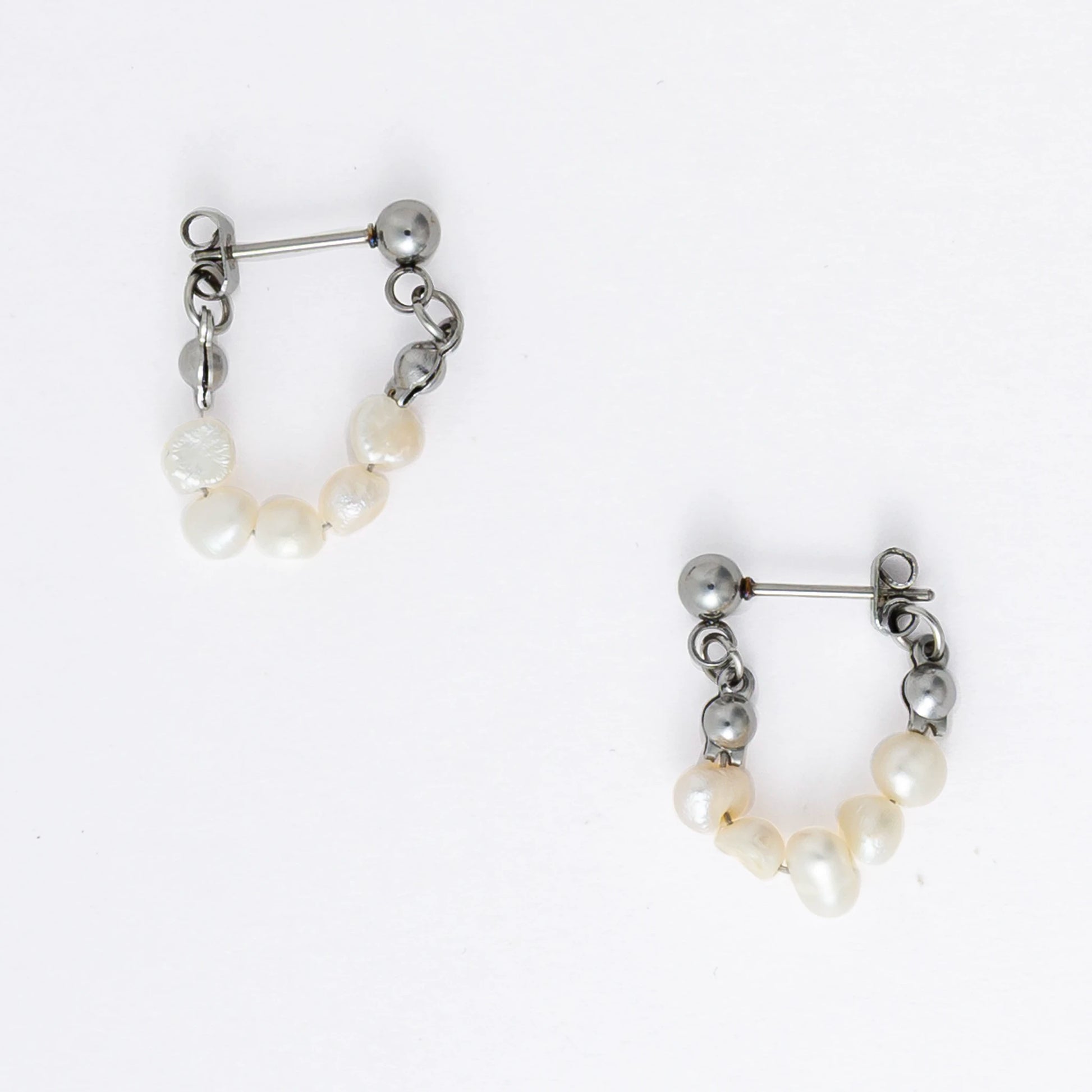 A pair of silver-colored thin pearl hoop earrings, displayed against a white background