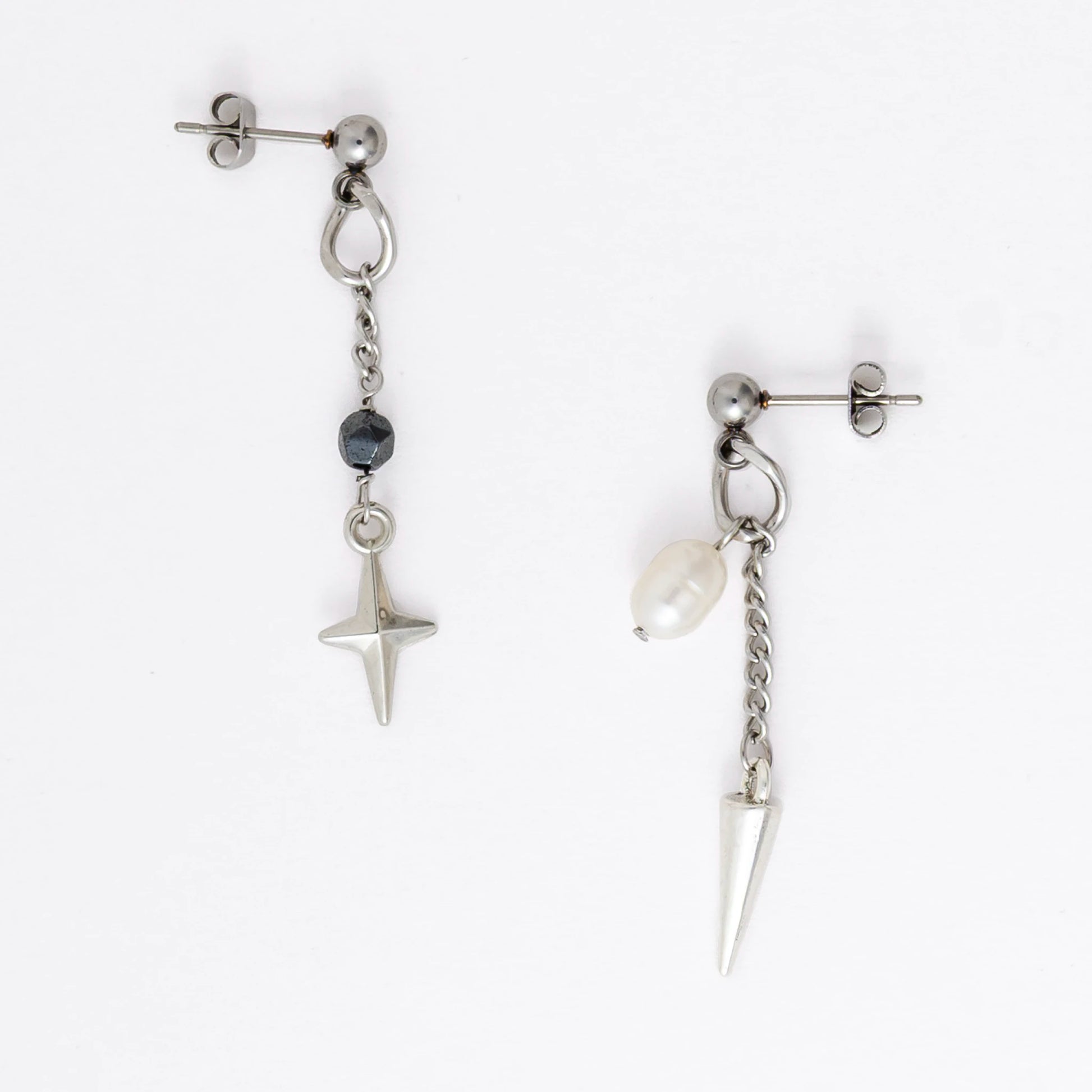Pair of silver stainless steel ball stud drop earrings with a chain and star charm and a pearl and spike charm on a white background