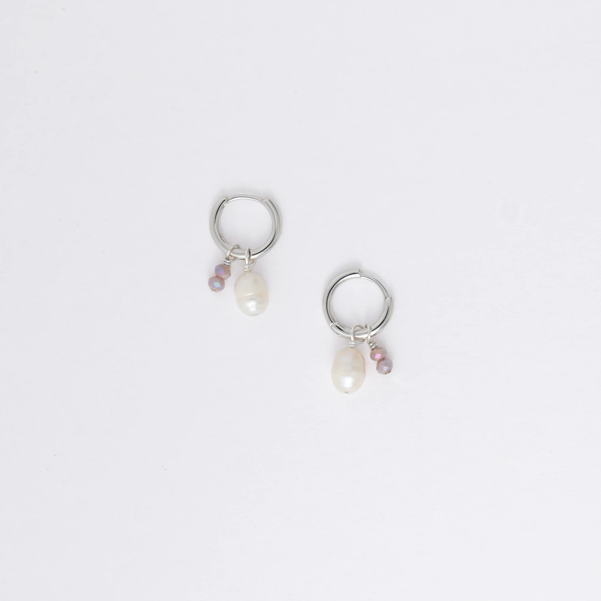 Pair of silver hoop earrings with pearl and gemstone charms on a light gray background