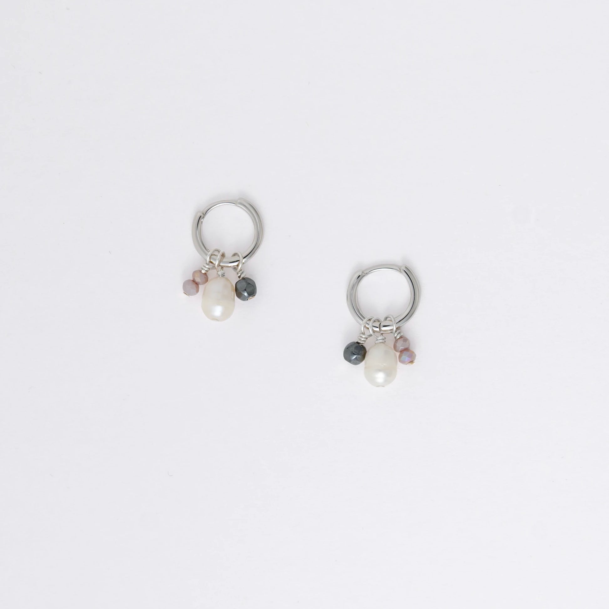 Pair of silver hoop earrings with pearl and gemstone charms on a light gray background