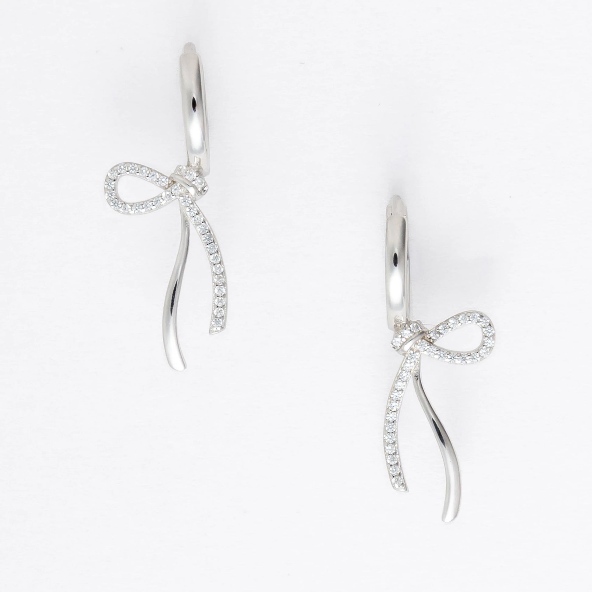 Pair of silver earrings with bow design on a light gray background