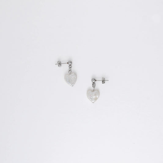 A pair of silver drop earrings featuring heart-shaped white pearls attached to the ends of long silver chains, displayed against a white background.