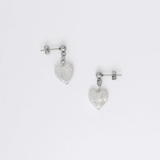 A pair of silver drop earrings featuring heart-shaped white pearls attached to the ends of long silver chains, displayed against a white background.