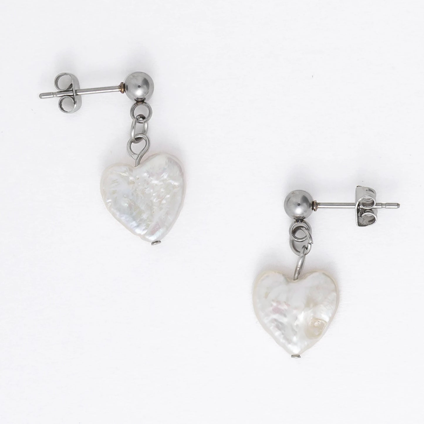 A pair of silver drop earrings featuring heart-shaped white pearls attached to the ends of long silver chains, displayed against a white background.