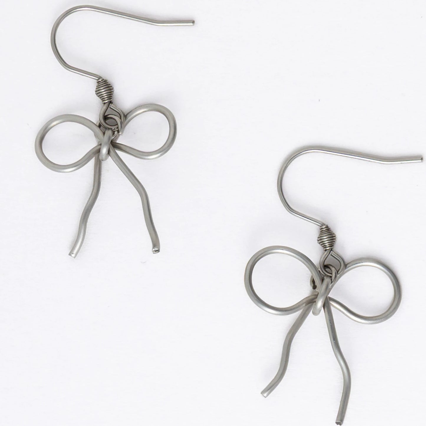 A pair of silver-toned ribbon bow drop earrings on a white background.