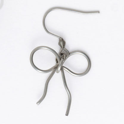 A pair of silver-toned ribbon bow drop earrings on a white background.