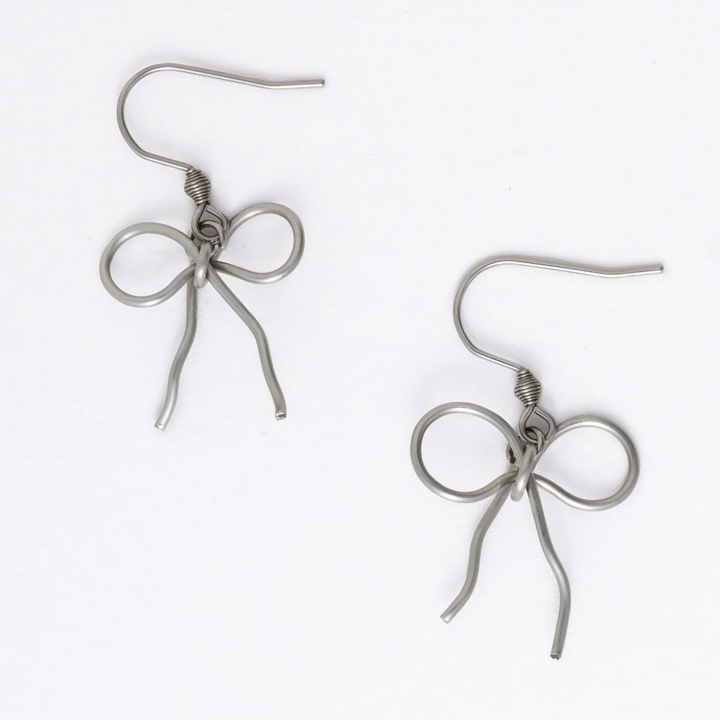 A pair of silver-toned ribbon bow drop earrings on a white background.