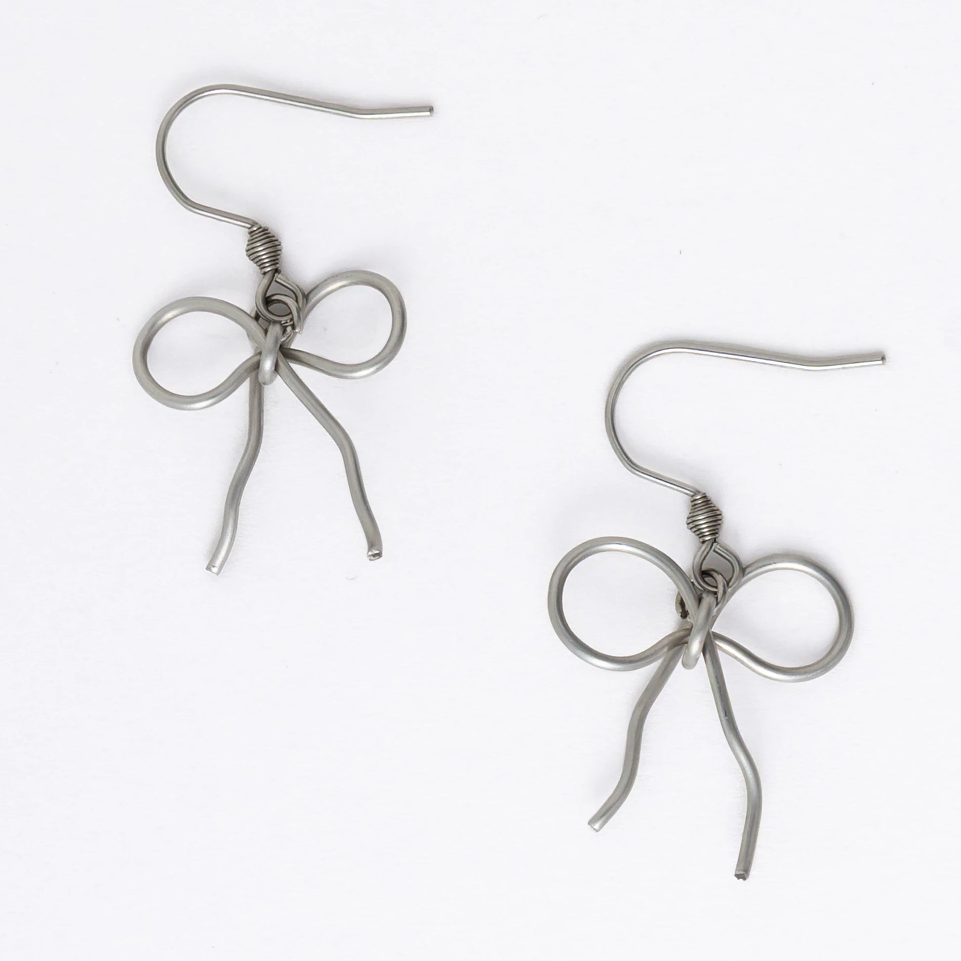 A pair of silver-toned ribbon bow drop earrings on a white background.