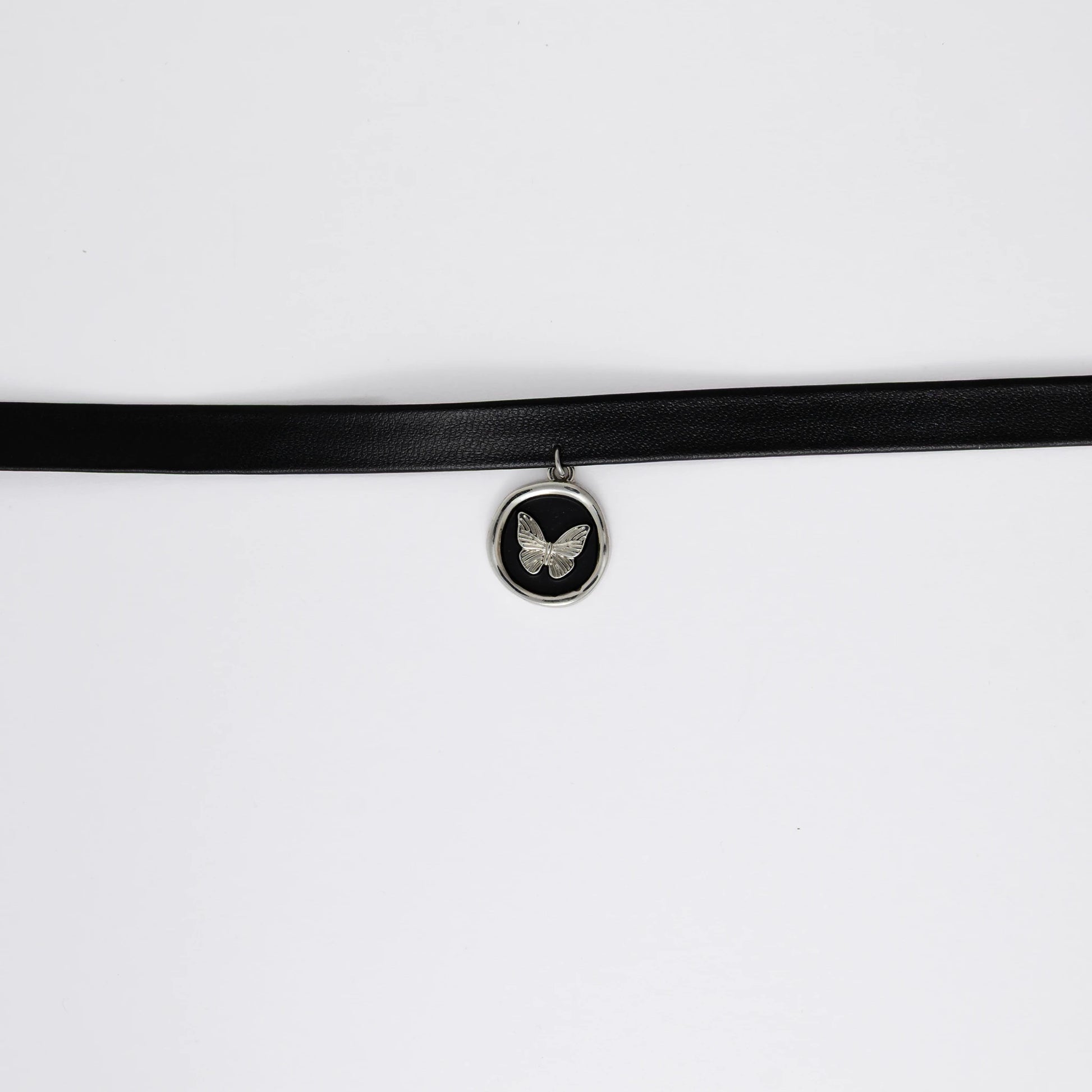 A black leather choker necklace with a central butterfly stamp pendant, displayed against a white background