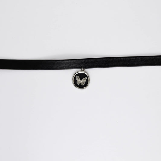 A black leather choker necklace with a central butterfly stamp pendant, displayed against a white background