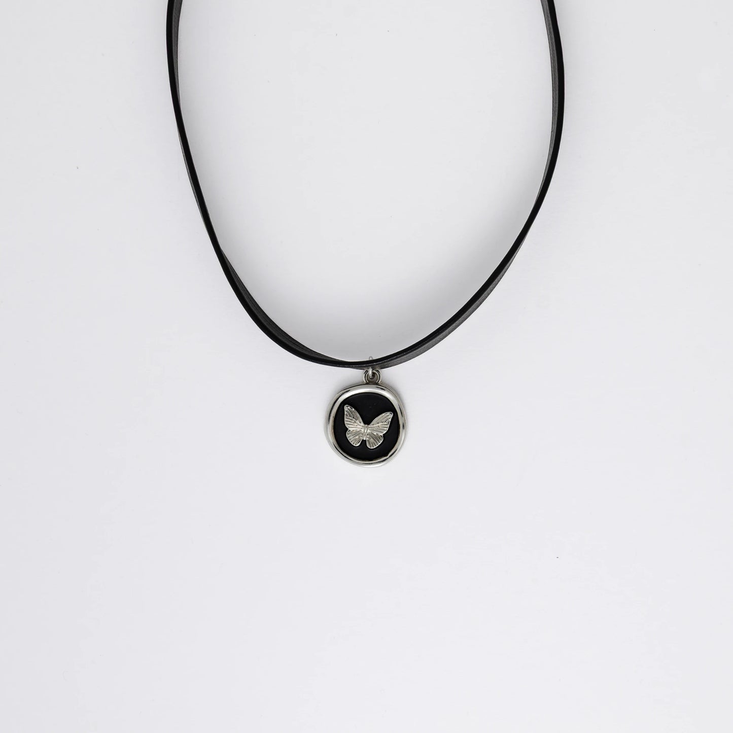 A black leather choker necklace with a central butterfly stamp pendant, displayed against a white background
