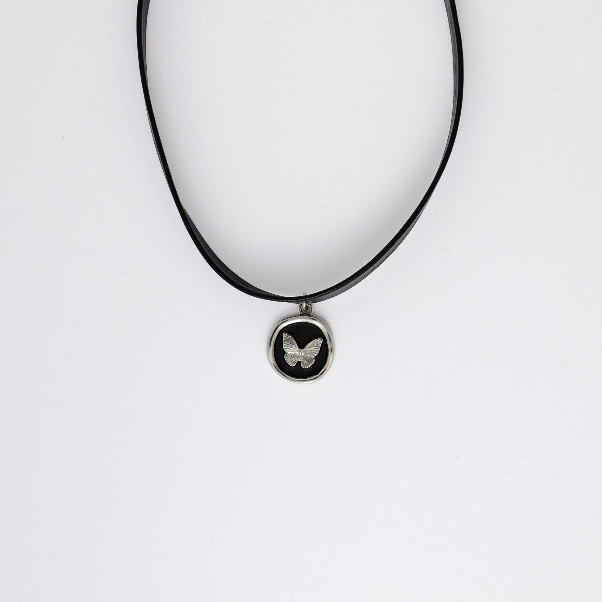 A black leather choker necklace with a central butterfly stamp pendant, displayed against a white background