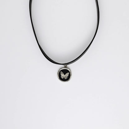 A black leather choker necklace with a central butterfly stamp pendant, displayed against a white background