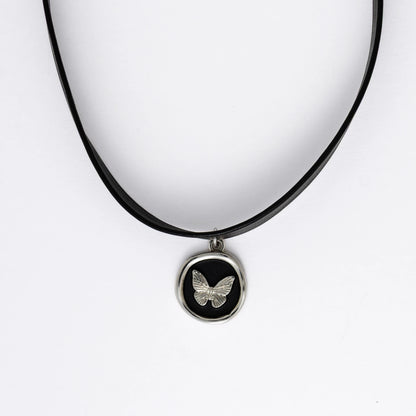 A black leather choker necklace with a central butterfly stamp pendant, displayed against a white background