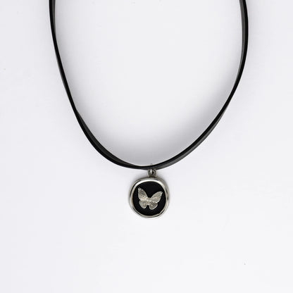 A black leather choker necklace with a central butterfly stamp pendant, displayed against a white background