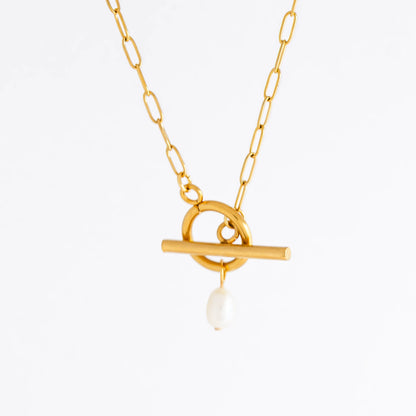 Gold paperclip necklace with toggle clasp and a pearl pendant on a light gray background